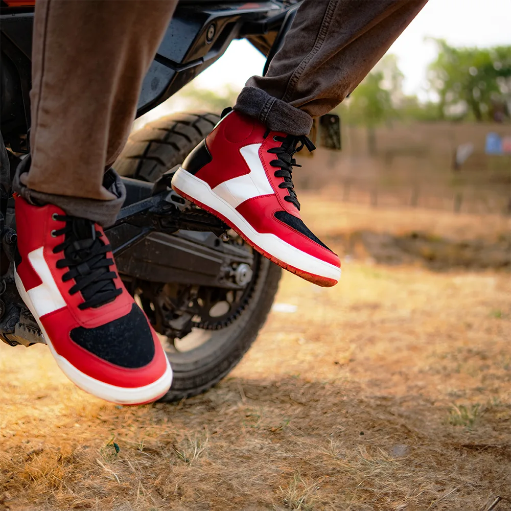 Red and black sneakers with white accents worn by a person on a motorcycle in an outdoor setting.
